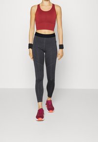 Czerwona sportowa croptop, czarne legginsy z wysokim stanem z teksturowanymi szwami oraz bordowe sneakersy z pomarańczowymi akcentami. Gładki materiał we wszystkich elementach.