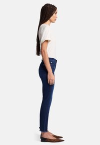 Wąskie jeansy w ciemnoniebieskim dżinsie z postrzępionym dołem, zestawione z jasnym, kremowym t-shirtem. Obuwie charakteryzuje się szpiczastym noskiem i wzorem w panterkę.