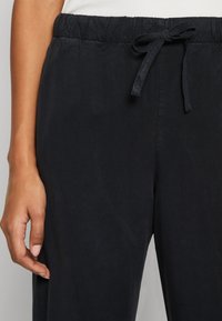 Black, lightweight pants with an elastic waistband and adjustable tie. Smooth texture with a relaxed fit. Visible hand resting on leg.