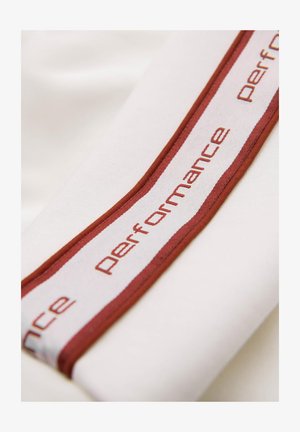 Hvidt stof med et bordeaux- og hvidstribet bånd, der indeholder ordet "performance" i gentaget tekst. Glat tekstur, minimalistisk design.