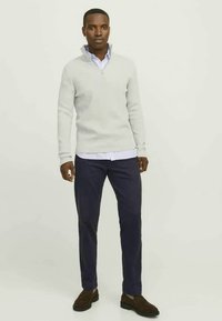 Light gray zip-up sweater with ribbed texture, layered over a collared blue shirt, paired with dark navy trousers and brown shoes.