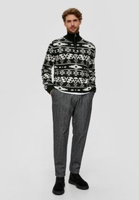 Schwarz-weißer gemusterter gestrickter Pullover mit Reißverschlusskragen, kombiniert mit grauen strukturierten Hosen und schwarzen Stiefeletten.