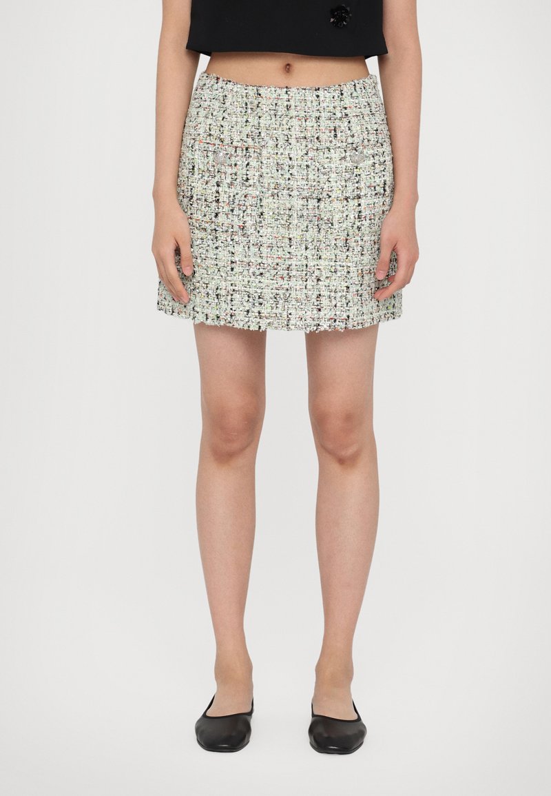 Tweed mini skirt in multicolored fabric with a textured finish, featuring a straight cut and subtle fringed hem. Worn with black flats.