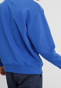 Felpa blu con collo rotondo, polsini e vita a costine. Realizzata in morbido tessuto misto cotone con un colore uniforme.