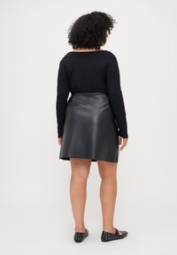 Top negro de manga larga combinado con una falda de piel sintética negra, con una textura suave y diseño en A, llevada con zapatos planos negros con tachuelas.