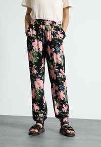 Svarta blommiga byxor med rosa och gröna tropiska mönster, elastisk midja, sidofickor och avsmalnande mudd, parat med svarta sandaler.