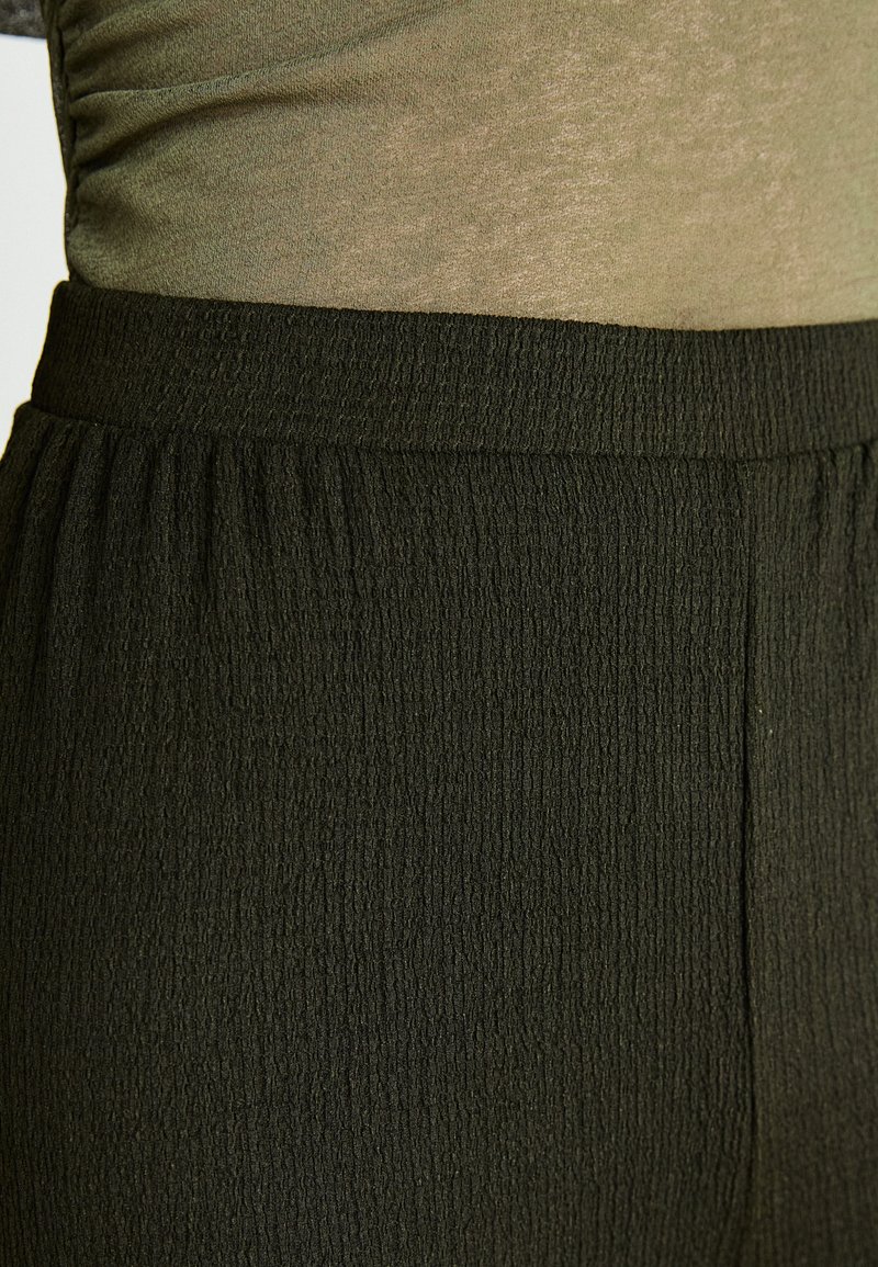 Elastischer Bund, strukturiert schwarzer Stoff mit Faltenmuster, entworfen für Komfort und Bewegungsfreiheit. Eignet sich für verschiedene Anlässe.