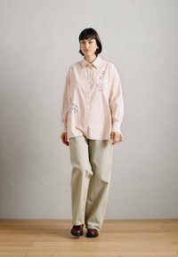 Ανοιχτό ροζ πουκάμισο με κεντημένα λουλούδια, συνδυασμένο με χαλαρούς, μπεζ παντελόνες και καφέ, επίπεδες γόβες. Λείο ύφασμα, χαλαρή εφαρμογή.