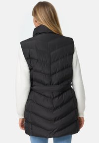 Mustapuffatakki, jossa on viistekuviointi, korkea kaulus, vyötärölle sidottu vyö, pehmeä rakenne ja valkoiset hihat, jotka kurkistavat alta.