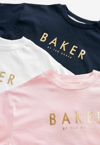 Kolme t-paitaa, tummansininen, valkoinen ja vaaleanpunainen. Jokaisessa on kultainen "BAKER"-tekstitys, klassinen pyöreä kaula-aukko ja pehmeä puuvillainen rakenne.