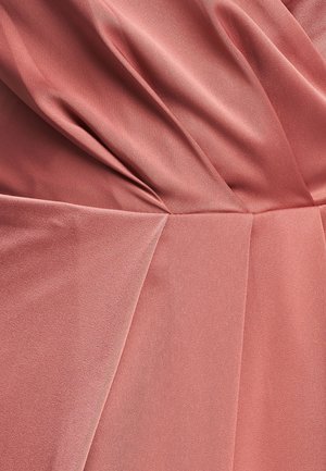 Ružičasta obleka iz prahu, ki se ponaša z mehkimi, tekočimi tkaninami z nagubanimi naborki in anguliranimi šivi, kar ustvarja teksturo in volumen v celotni zasnovi.