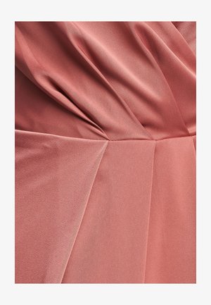 Ružičasta obleka iz prahu, ki se ponaša z mehkimi, tekočimi tkaninami z nagubanimi naborki in anguliranimi šivi, kar ustvarja teksturo in volumen v celotni zasnovi.