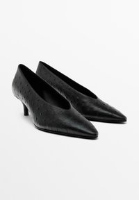 Ett par svarta pumps med spetsig tå och låg klack för kvinnor, med en texturerad prickig mönstring på släta lädermaterial.
