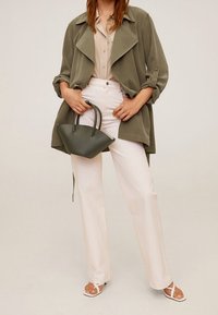 Olive green oversized jacket, jasny beżowa koszula, kremowe szerokie spodnie, białe sandały oraz mała ciemnozielona torebka na dwa uchwyty.