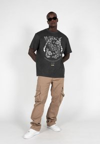 Charcoal graphic t-shirt with white floral design, paired with beige cargo pants featuring side pockets and white sneakers. Dark sunglasses worn.