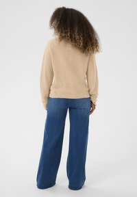 Maglione a maglia beige con scollo a V e maniche lunghe, abbinato a jeans in denim blu a gamba larga. Tessuto morbido e vestibilità rilassata.