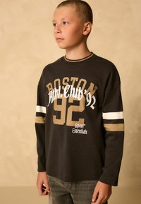 Černé tričko s dlouhým rukávem s potiskem "BOSTON 92", světle hnědými akcenty a bílými pruhovanými rukávy. Materiál vypadá měkce a mírně texturovaně.