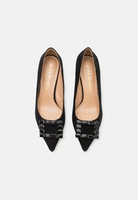 Decolté nere in suede con punta a mandorla e un'abellimento geometrico nero lucido sulla parte anteriore; fodera interna color beige con testo del marchio in oro.
