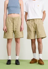 Khaki shorts with elastic waistband and drawstring, featuring large pockets, paired with a cropped denim top and a plain white t-shirt.