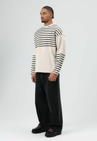 Chemise crème à manches longues avec des rayures horizontales noires, associée à un jean noir à jambes larges et des chaussures noires à lacets roses.