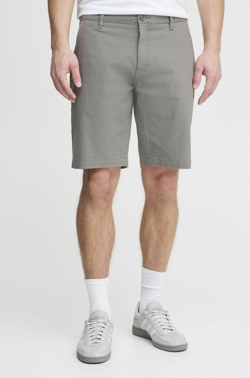 Shorts en coton gris avec une coupe droite, passants de ceinture, fermeture à bouton et poches latérales ; portés avec des baskets grises et des chaussettes blanches.