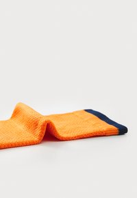 Calzino arancione brillante con una superficie texturizzata, caratterizzato da un polsino blu navy solido nella parte superiore. Il calzino è piegato, mettendo in mostra la sua forma.