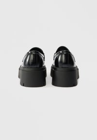 Black patent leather shoes with thick black soles. Features include a rounded toe and subtle stitching details on the upper.