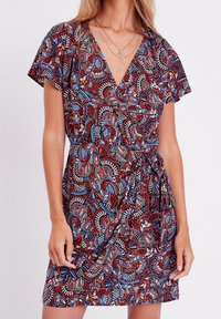 Robe portefeuille à fleurs rouges et bleues avec manches courtes, encolure en V et détail de taille froncée. Présente un tissu à motif et une longueur jusqu'aux genoux.