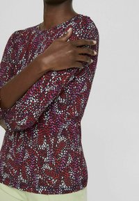 Långärmad topp i röd och lila mönster med rund halsringning, som har ett strukturerat material och elastisk finish vid ärmarna.