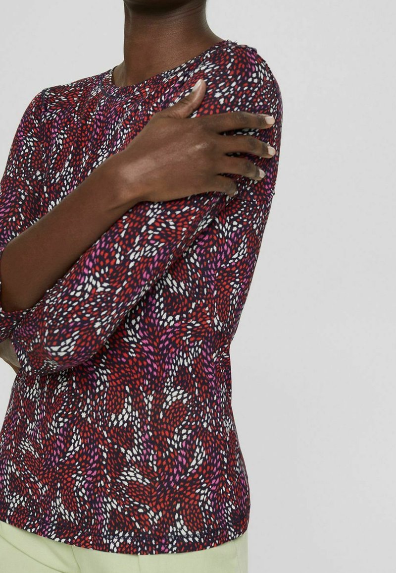 Långärmad topp i röd och lila mönster med rund halsringning, som har ett strukturerat material och elastisk finish vid ärmarna.