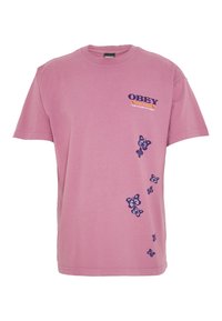 Růžové bavlněné tričko s fialovým nápisem "OBEY" na levé straně hrudi a motivy motýlů podél boku. Klasický střih s kulatým výstřihem.