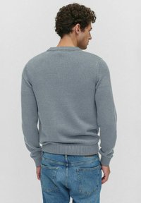 Grijze gebreide trui met een ribbelkraag en boorden, met een aansluitend ontwerp. Gekozen over blauwe spijkerbroek, wat een casual uitstraling geeft.