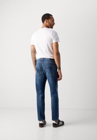 Jeans din denim albastru cu croi drept, cinci buzunare, cusături vizibile și o ușoară decolorare, purtate cu un tricou alb simplu și pantofi negri.
