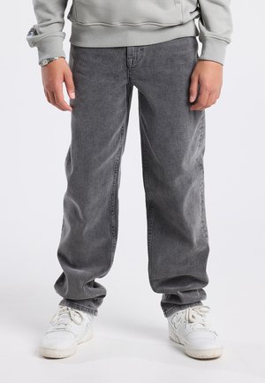 Grijze denim broek met een relaxte pasvorm, met een gestructureerd oppervlak. Gecombineerd met witte sneakers, zichtbaar met veters en een iets versleten uitstraling.
