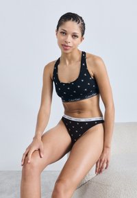 Σετ αθλητικό σου τιέν και στρινγκ από μαύρο βαμβάκι με μοτίβο λογότυπου σε όλη την επιφάνεια και λευκή ελαστική ζώνη στη μέση. Λείος υφασμάτινος, εφαρμοστός σχεδιασμός.