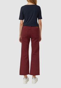 Bordeaux brede broek met een rafelige zoom, gecombineerd met een marineblauwe shirt, gezien vanaf de achterkant. Zilveren platform sneakers. Eenvoudig, casual ontwerp.