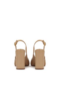Beige Slingback-Pumps mit Blockabsätzen und verstellbaren goldfarbenen Schnallenriemen, von hinten auf weißem Hintergrund betrachtet.