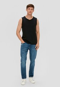 Zwarte mouwloze T-shirt, relaxte pasvorm, gecombineerd met blauwe denim spijkerbroek en witte sneakers. Glad materiaal, casual ontwerp, neutrale achtergrond.