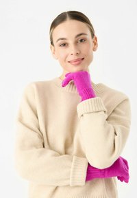 Felgekleurde roze gebreide handschoenen met geribbelde manchetten, gedragen door een persoon in een beige trui, die textuur en kleurcontrast laat zien.
