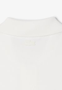 Polo blanc en tissu texturé, doté d'un col côtelé et d'un logo discret brodé de la même couleur dans le dos.