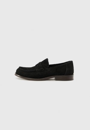 Mocassini in suede nero con punta arrotondata, tacco basso e dettagli cuciti sulla tomaia. Fodera interna liscia e una sottosola marrone discreta.
