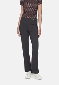 Schwarze, eng anliegende Hosen aus texturiertem Stoff mit einem glatten Bund und dezenten vorderen Bügelfalten, kombiniert mit weißen Turnschuhen.