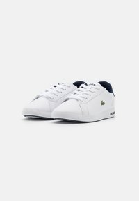 White sneakers with a smooth synthetic material, rounded toe, lace-up front, navy accents on the tongue, and a logo on the side.