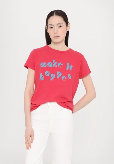 Red cotton t-shirt featuring blue text that reads "make it happen," short sleeves, and a round neckline, styled with white jeans.