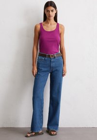 Dopasowany, prążkowany fioletowy top na ramiączkach w połączeniu z wysokoosadzonymi, prostymi niebieskimi dżinsami. Brązowy pasek i płaskie sandały dopełniają stylizację.