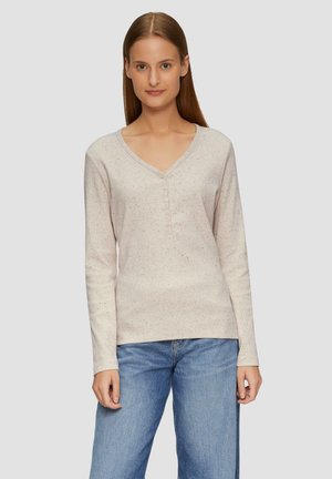 Langemouwige, lichtbeige top met een V-hals, knoopsluiting en een gespikkelde textuur. Gecombineerd met loszittende blauwe jeans.