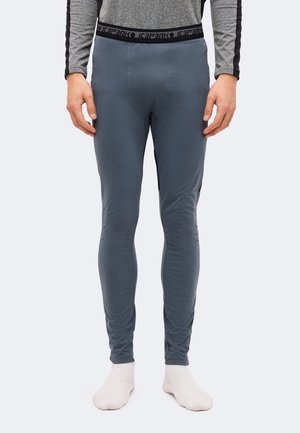 Un mannequin porte un legging thermique ajusté gris foncé, doté d’une ceinture noire siglée, sur un fond clair uni.
