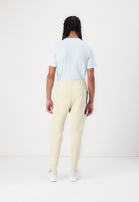 Hellblaues Kurzarm-T-Shirt, kombiniert mit eng anliegenden, cremefarbenen Jogginghosen, die über eine seitliche Reißverschlusstasche und gerippte Bündchen verfügen. Weiße Sneakers runden den Look ab.