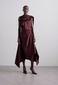Burgundi satiinkleit asümmeetrilise drapeeringu ja ühe õlaga kujundusega, paari mustade terava ninaga kingadega. Sile tekstuur ja elegantne siluett.