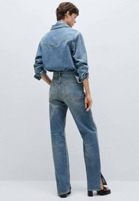 Denim jakna in hlače z visokim pasom, obe v svetlo modri barvi. Jakna ima ovratnik s kratkimi rokavi in zvite rokave. Hlače imajo stranske razpoke pri gležnjih.